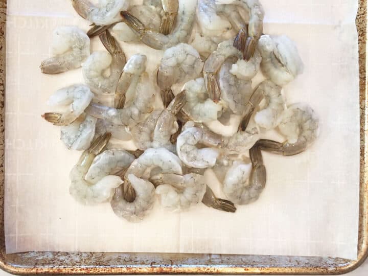 Raw shrimp arranged on a baking sheet.