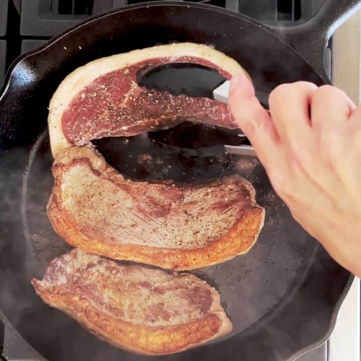 Flipping the steaks with tongs.