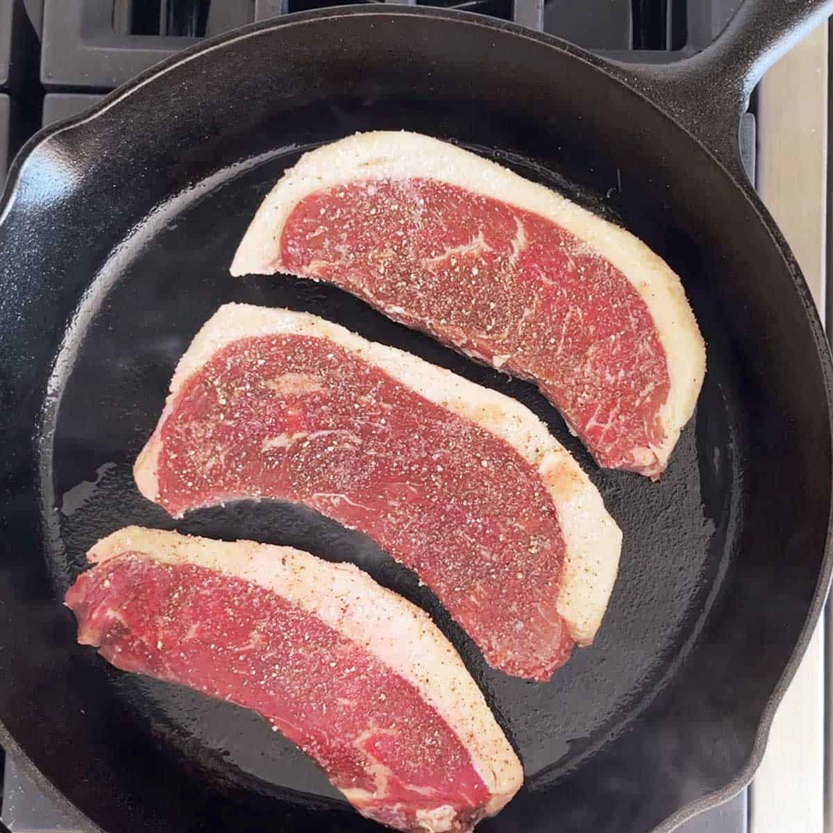 Three picanha steaks in a cast-iron skillet.