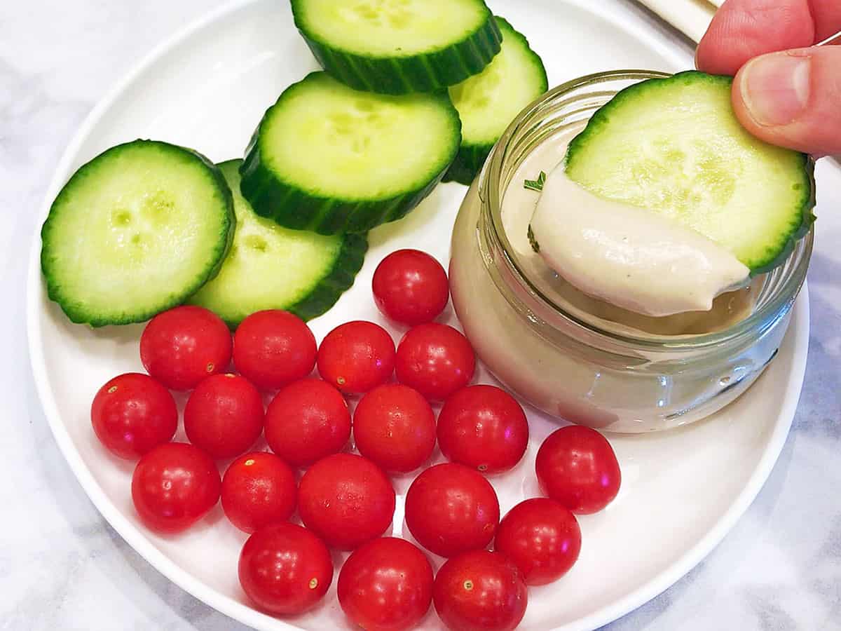 Dipping a cucumber slice into a bowl of tahini sauce.