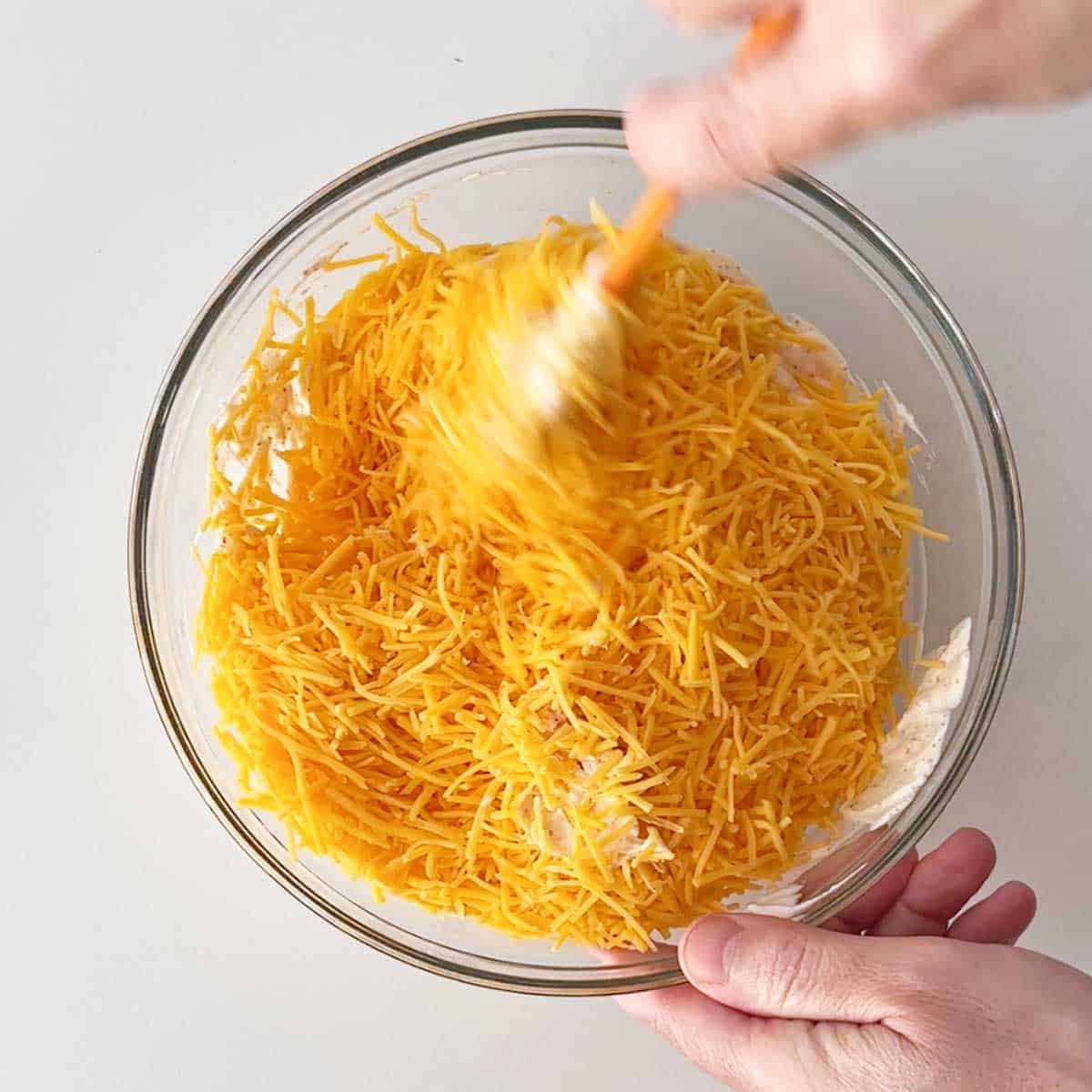 Adding shredded cheese to cream cheese dip.