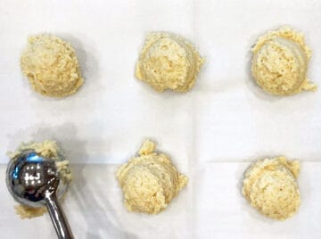 Six mounds of biscuit batter on a baking sheet.