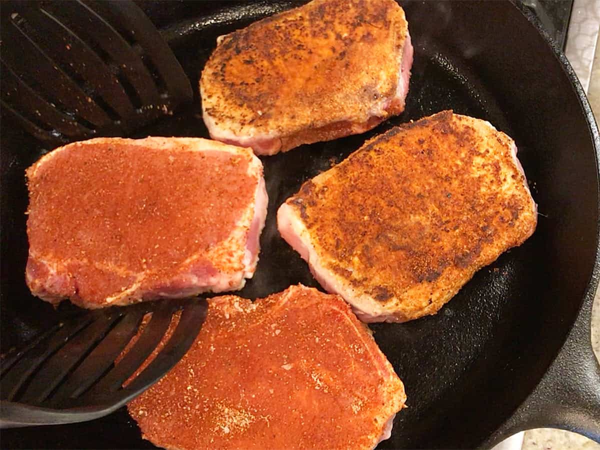 Searing pork chops in a cast-iron skillet before placing them in the oven.