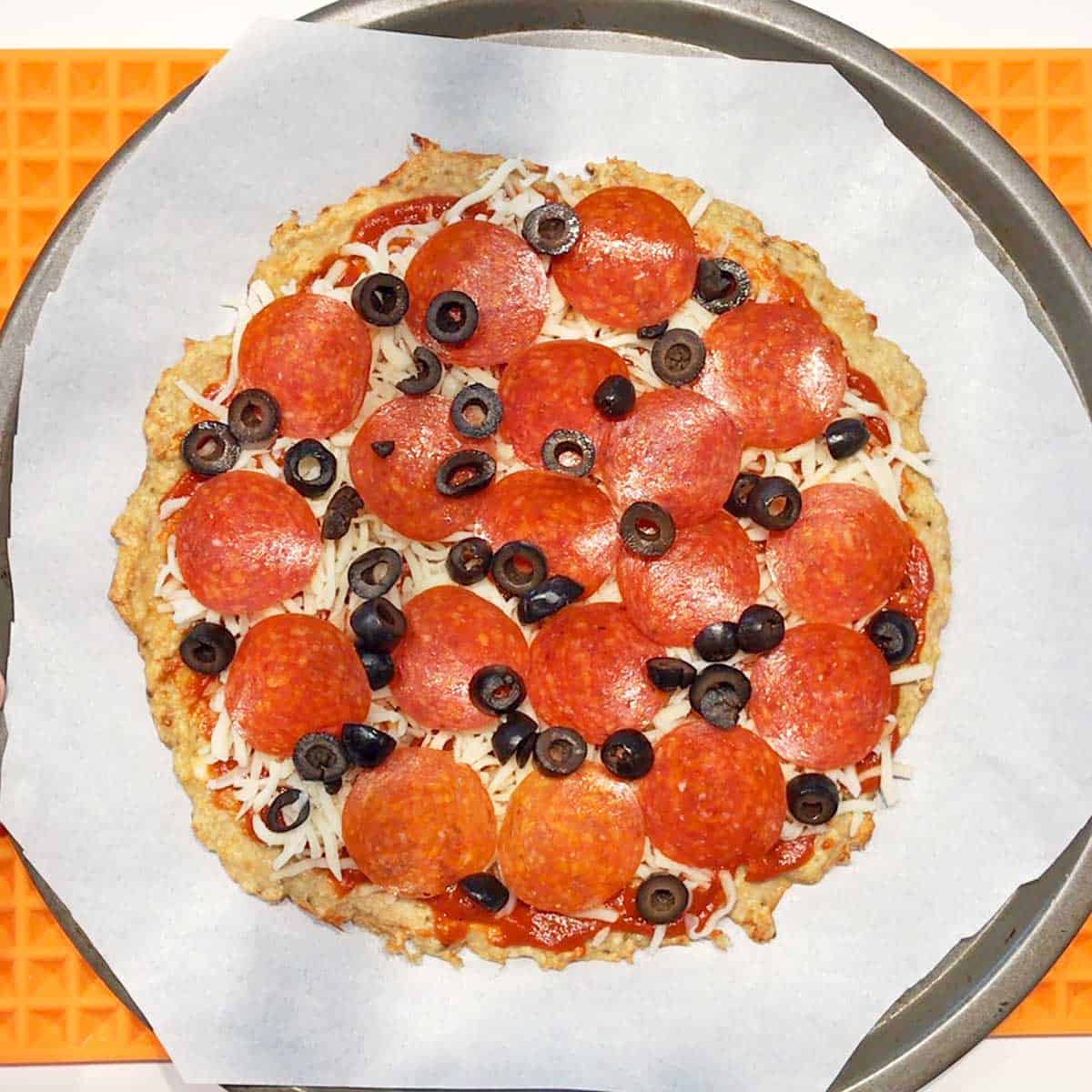 Baked chicken crust with toppings on a pizza pan.