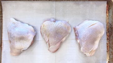 Raw chicken thighs arranged on a baking sheet.