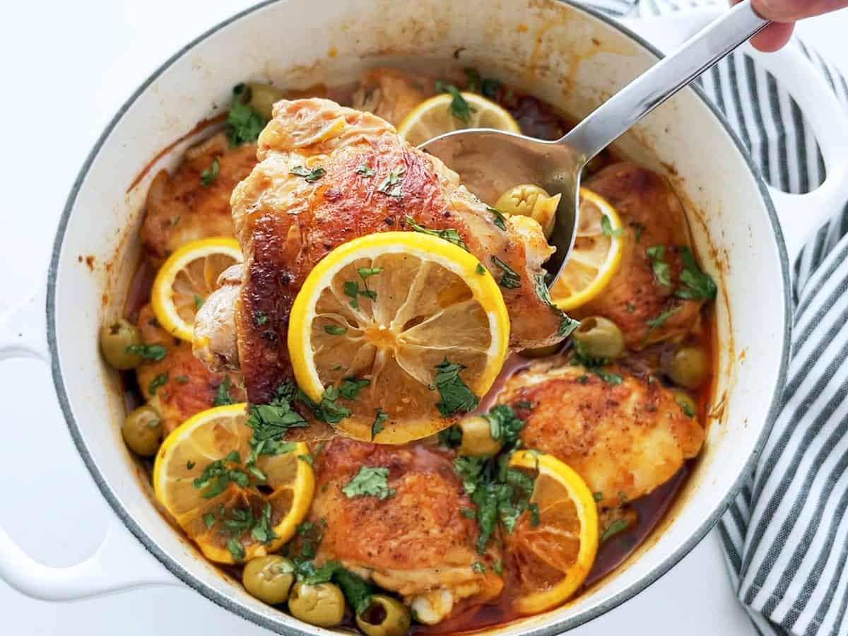 The dish is ready in the saucepan. A serving spoon lifts a piece of chicken up.