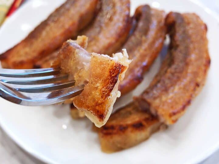 A fork holding a piece of pork belly.