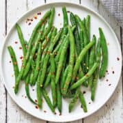 Sauteed green beans are served on a white plate with a napkin.