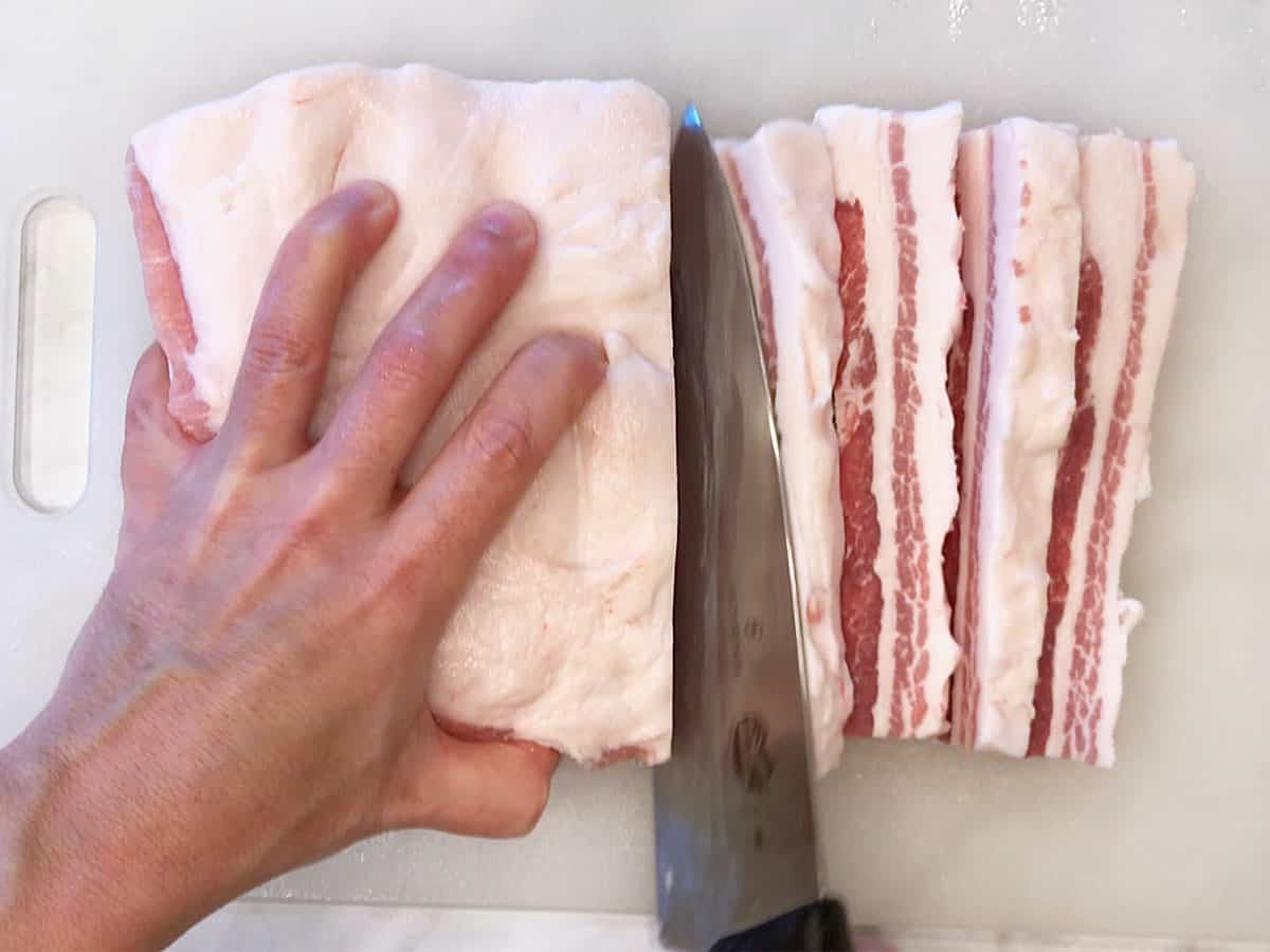 Slicing a whole pork belly into strips.