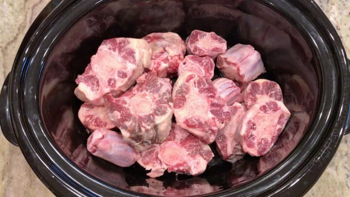 Raw oxtails in a slow cooker pan.