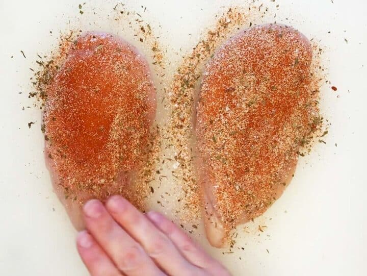 Seasoning chicken breasts with Cajun spices.