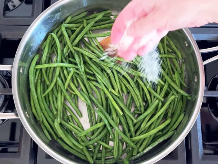 Seasoning haricot verts with kosher salt.