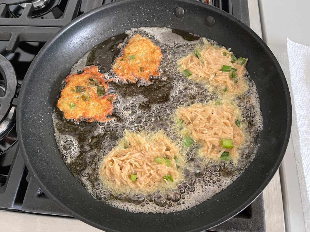 Adding more latkes to the skillet.