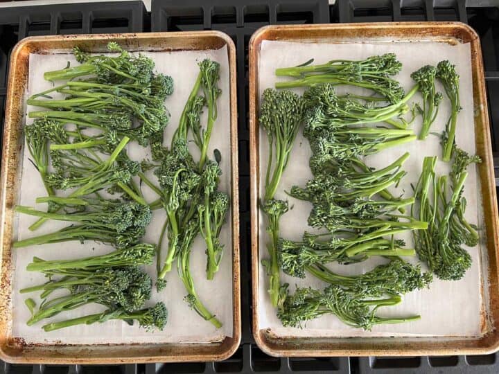 Raw broccolini on two parchment-lined, rimmed baking sheets.