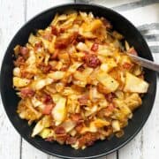 Fried cabbage is served in a bowl with a spoon and a napkin.