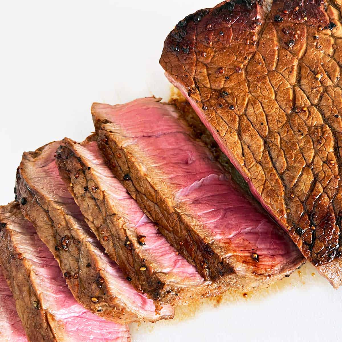London broil steak is sliced and served on a white cutting board.