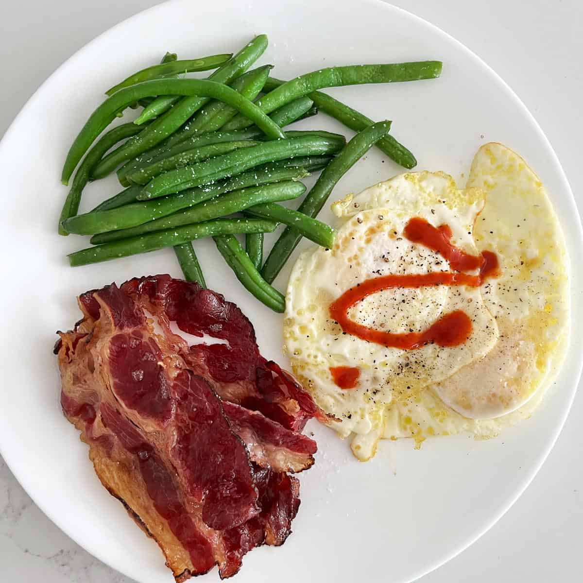 Beef bacon is served with fries egg (over hard) and green beans.