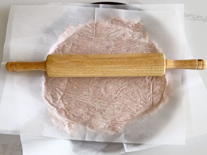 Using a rolling pin to spread the crust mixture on the pan.