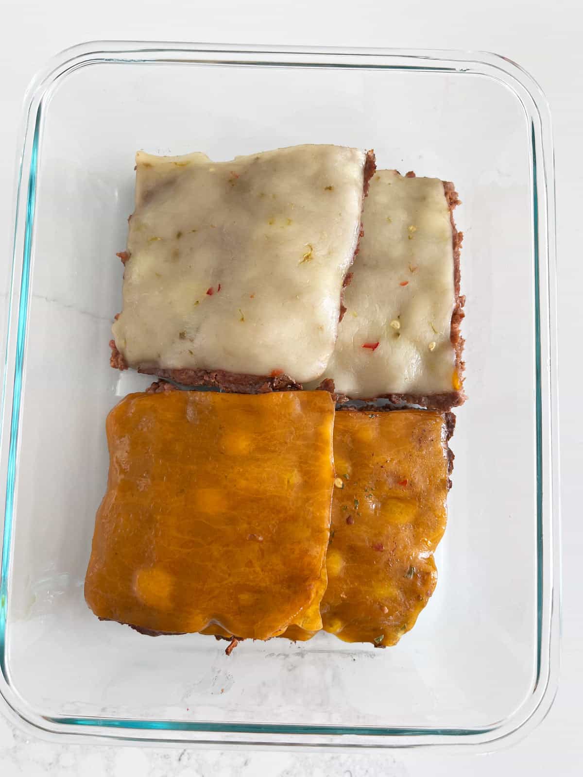 Baked hamburgers leftovers are stored in a glass food storage container.
