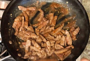 Adding the sauce to the beef in the skillet.