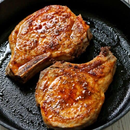 Two pork chops are served in a cast-iron skillet.