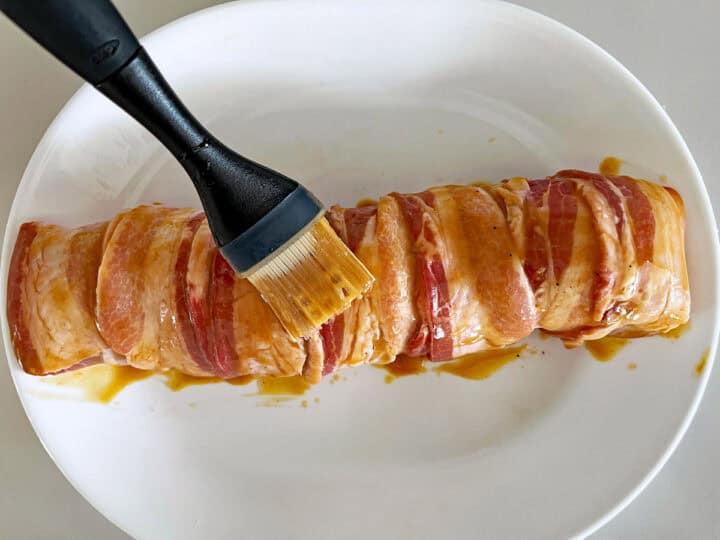 Brushing the tenderloin with sauce before baking it.