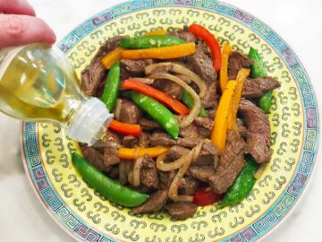 Drizzling the stir-fry with sesame oil.