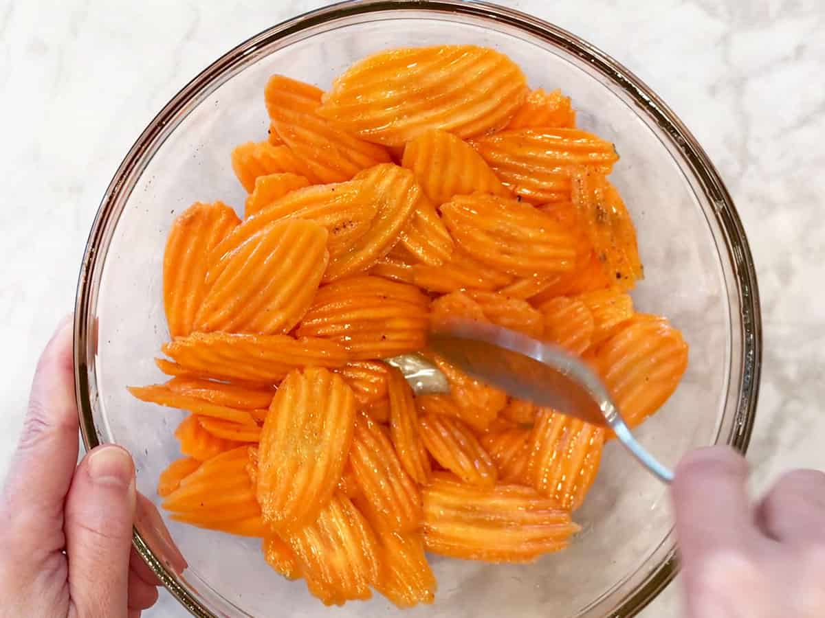Tossing the carrot slices with oil and spices in a bowl.