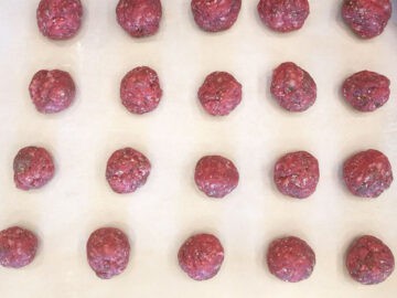 The meatballs are arranged on a parchment-lined baking sheet.