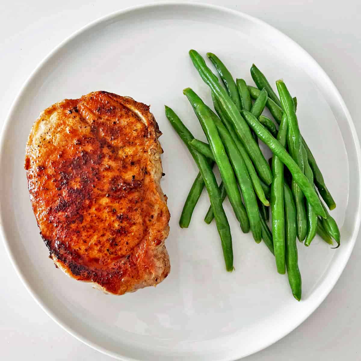 Leftover boiled green beans are served as a side to a pork chop.