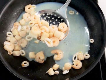 Removin the cooked seafood from the skillet with a slotted spoon.