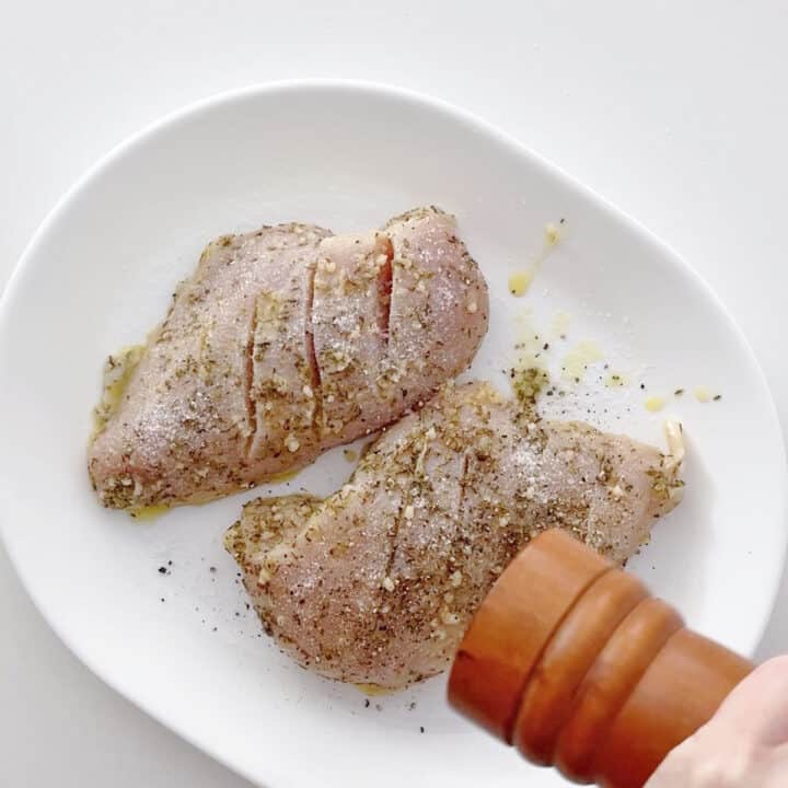 Seasoning the chicken with black pepper.