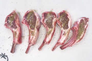 Seasoned lamb chops on a cutting board.