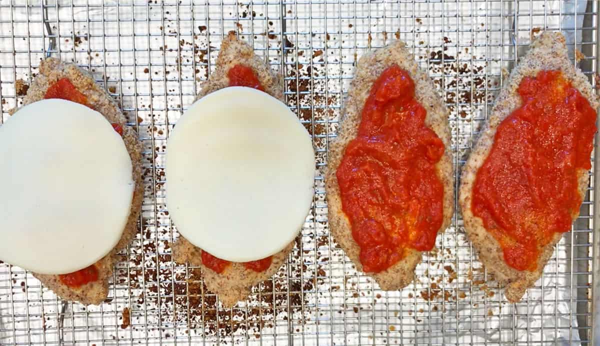 Topping the chicken with marinara sauce and cheese.