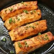 Four pieces of broiled salmon in a cast-iron skillet.