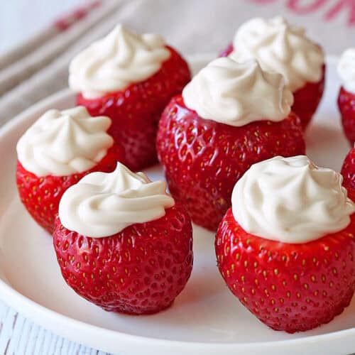 Cheesecake-stuffed strawberries are served on a white plate.