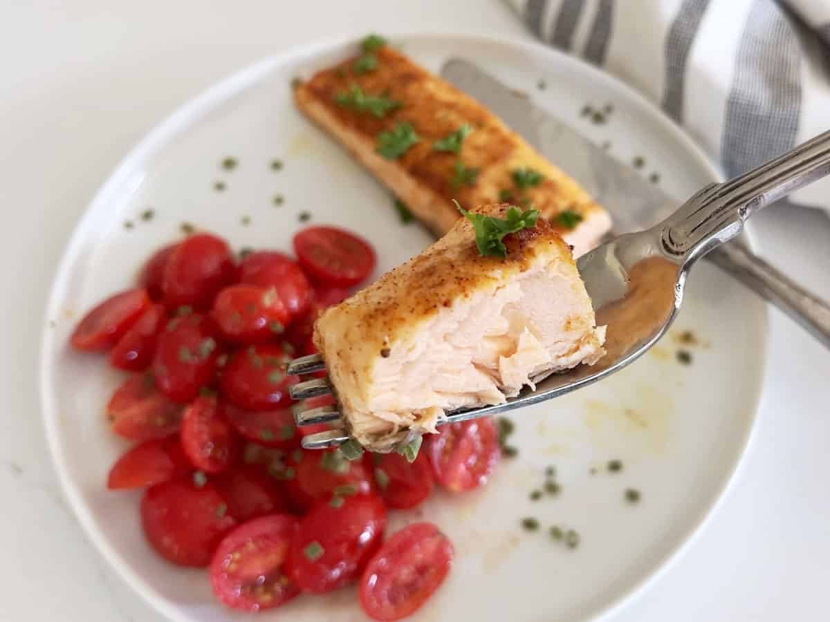 A fork showing off a piece of broiled salmon, which is perfectly cooked.