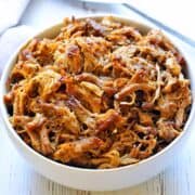 Slow cooker carnitas are served in a white bowl.