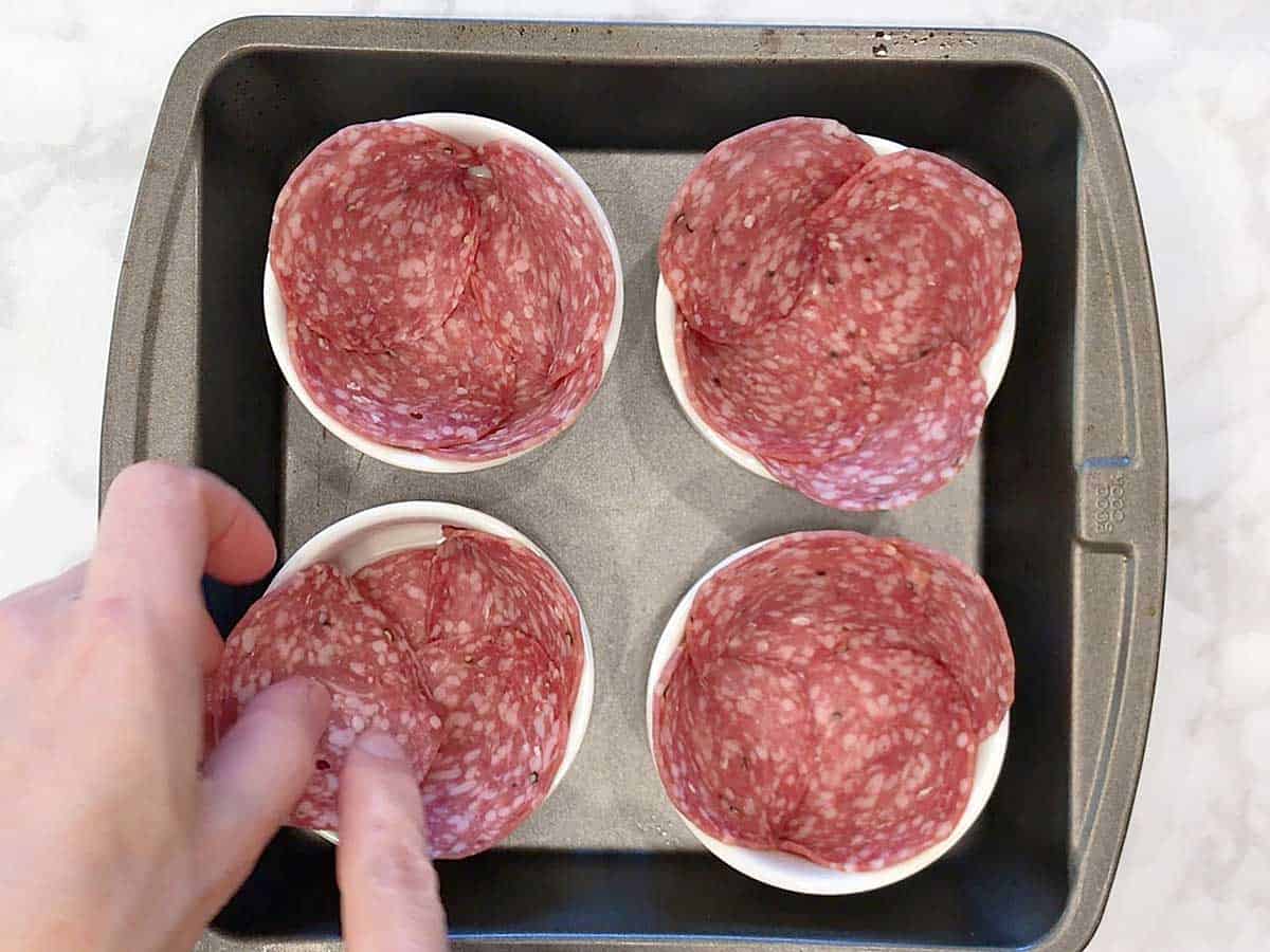 Arranging the salami slices in the ramekins.
