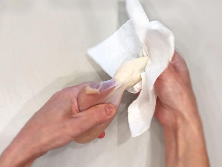 Using a paper towel to remove the skin off a chicken drumstick.