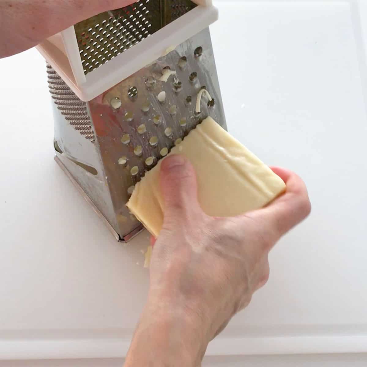 Shredding a block of cheese with a box grater.