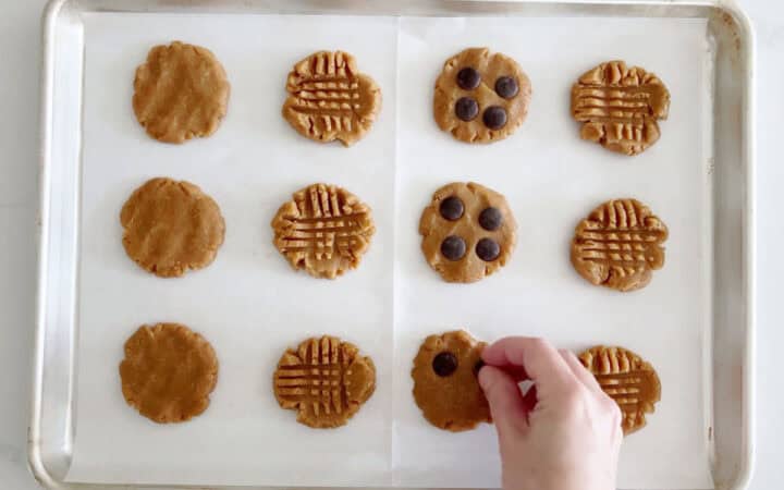 Adding chocolate chips to some of the cookies in the pan.