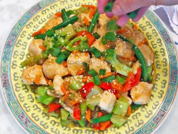 Garnishing the stir-fry with chopped scallions.