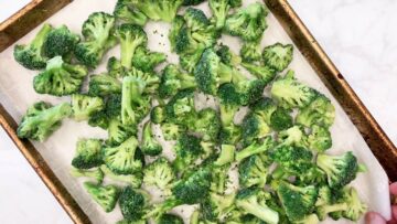 Frozen broccoli florets are arranged on a parchment-lined baking sheet.