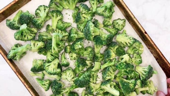 Frozen broccoli florets are arranged on a parchment-lined baking sheet.