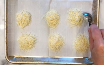 Six cheese mounds on a parchment-lined baking sheet.