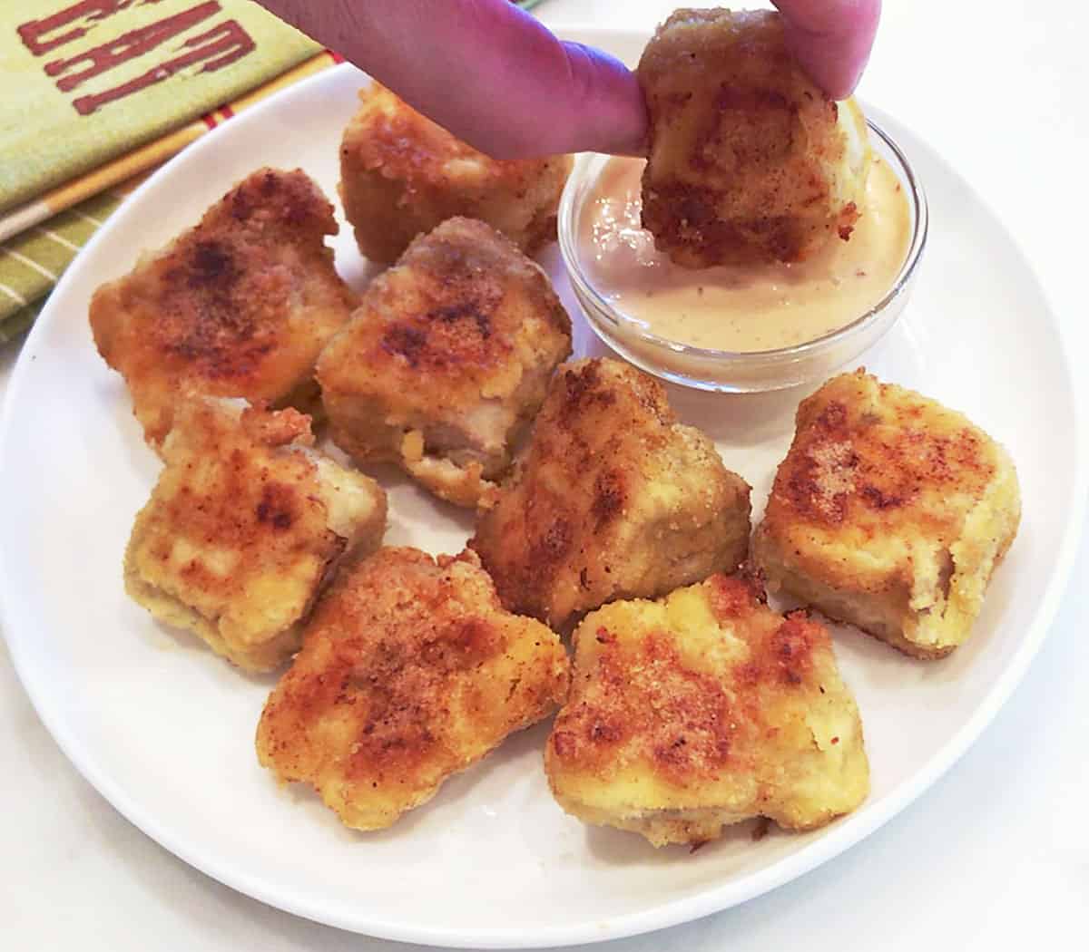 A keto chicken nugget is dipped into the dipping sauce.