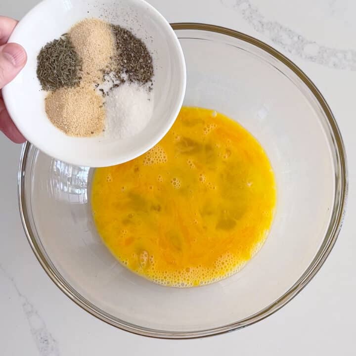 Adding spices to the eggs in a bowl.