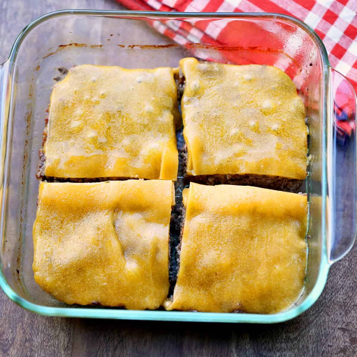 Baked hamburgers in a baking dish, topped with melted cheese.
