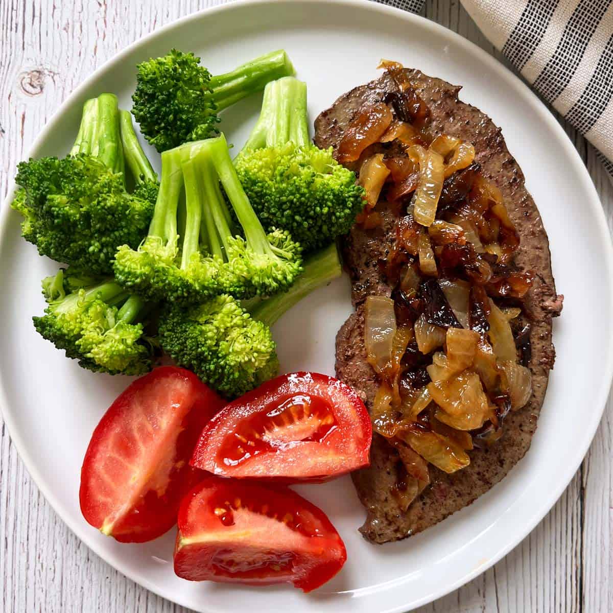 Beef liver is topped with caramelized onions and served with microwave broccoli and sliced tomatoes.